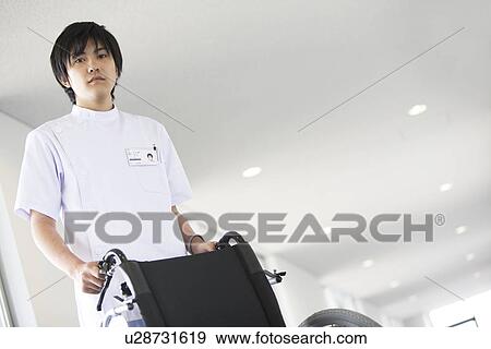 Stock Photo - Orderly pushing wheelchair in hospital. Fotosearch