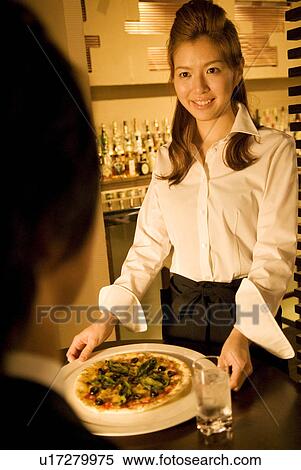Stock Photography - Waitress bringing a pizza to a table. Fotosearch