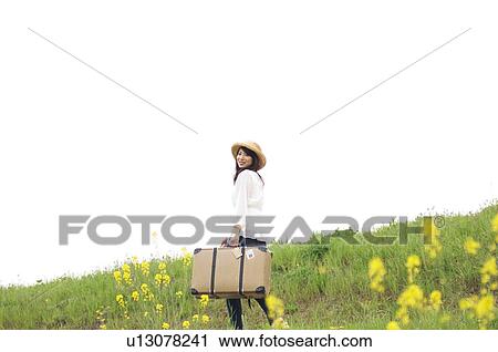Woman carrying suitcase walking through a meadow View Large Photo Image Stock Image - Woman carrying suitcase walking through a meadow. Fotosearch