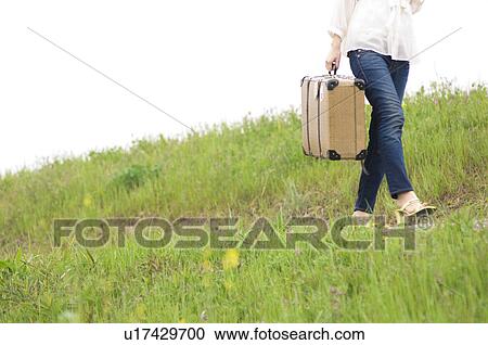 Woman carrying suitcase walking through a field View Large Photo Image Stock Image - Woman carrying suitcase walking through a field. Fotosearch