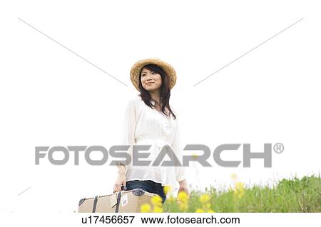 Stock Photo - Woman carrying suitcase walking through a meadow. Fotosearch