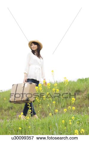 Woman carrying suitcase walking through a meadow View Large Photo Image Stock Photo - Woman carrying suitcase walking through a meadow. Fotosearch