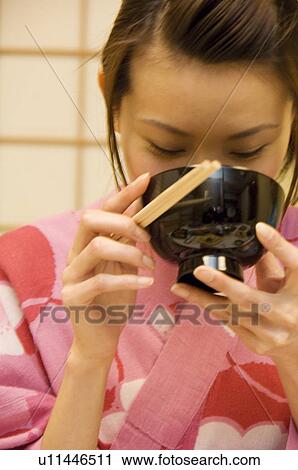 Stock Image - Woman dressed in a yukata and drinking miso soup. Fotosearch