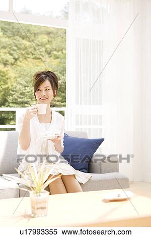 Woman drinking tea on sofa in living room View Large Photo Image Stock Photography - Woman drinking tea on sofa in living room. Fotosearch