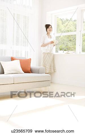 Stock Photo - Woman holding book in living room. Fotosearch