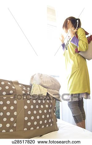 Stock Image - Woman looking out hotel room window. Fotosearch