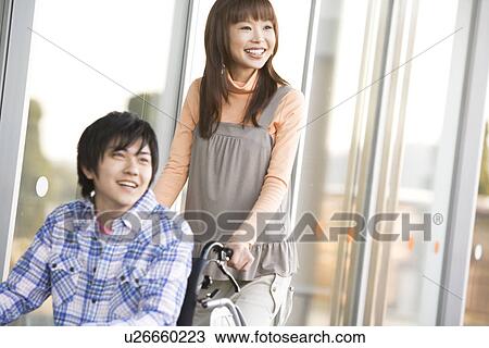 Stock Image - Woman pushing her boyfriend in a wheelchair. Fotosearch