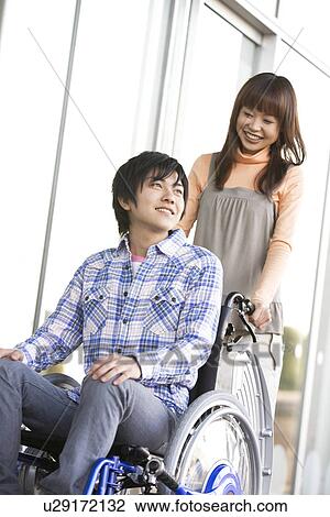 Stock Image - Woman pushing her boyfriend in a wheelchair. Fotosearch