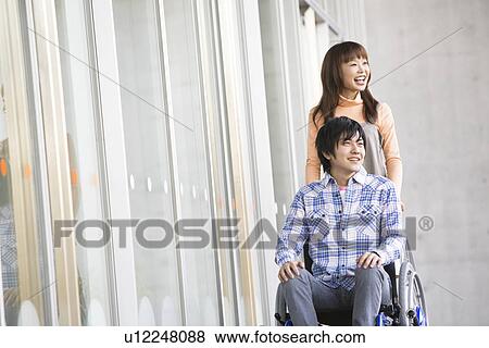 Stock Photo - Woman pushing her boyfriend in a wheelchair. Fotosearch