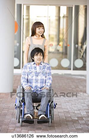 Stock Photograph - Woman pushing her boyfriend in a wheelchair. Fotosearch
