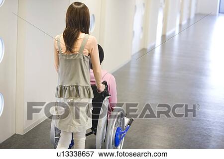 Stock Photo - Woman pushing her boyfriend who is in a wheelchair. Fotosearch