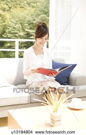 Picture - Woman reading book on sofa in living room. Fotosearch