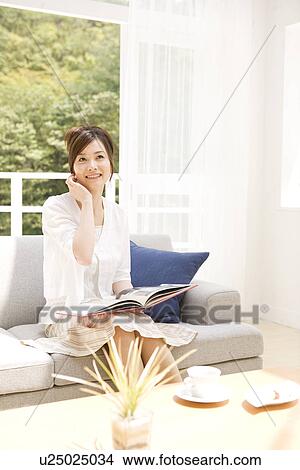 Woman reading book on sofa in living room View Large Photo Image Picture - Woman reading book on sofa in living room. Fotosearch