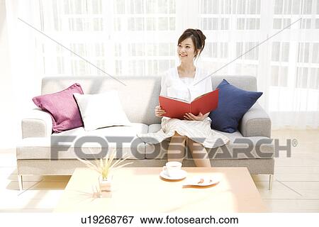 Woman reading book on sofa in living room View Large Photo Image Stock Photo - Woman reading book on sofa in living room. Fotosearch