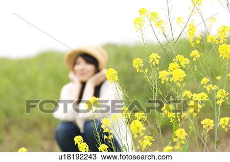 Stock Image - Woman sitting in field wearing straw hat. Fotosearch