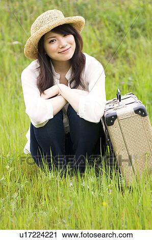 Stock Image - Woman sitting in field with suitcase. Fotosearch