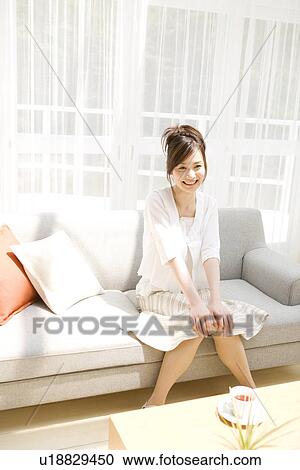 Stock Image - Woman sitting on sofa in living room. Fotosearch