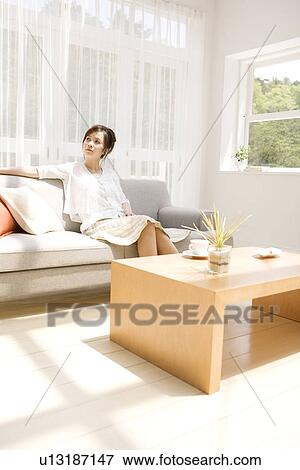 Stock Photo - Woman sitting on sofa in living room. Fotosearch