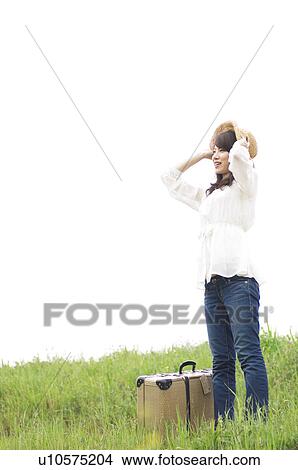 Woman standing in field with suitcase and putting on straw hat View Large Photo Image Picture - Woman standing in field with suitcase and putting on straw hat. Fotosearch