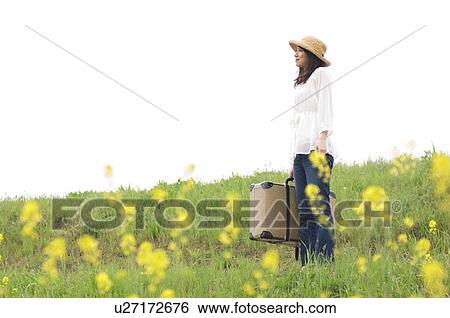 Stock Photograph - Woman standing in meadow with suitcase. Fotosearch