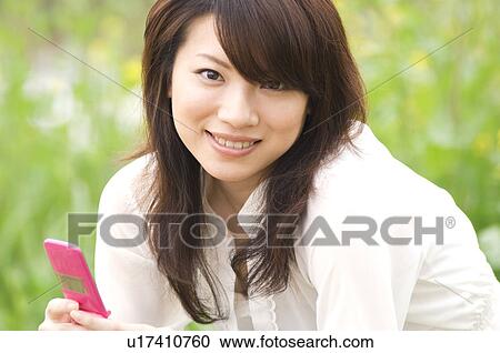 Stock Image - Woman texting on cellphone in a meadow. Fotosearch