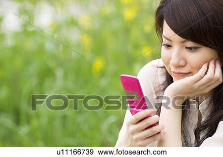 Woman texting on cellphone in a meadow View Large Photo Image Stock Photo - Woman texting on cellphone in a meadow. Fotosearch