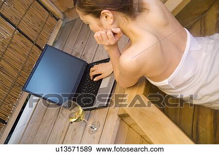 Stock Photo - Woman using her laptop and drinking wine in a hot tub. Fotosearch
