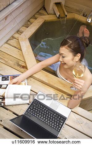 Stock Photograph - Woman using her laptop and drinking wine in a hot tub. Fotosearch