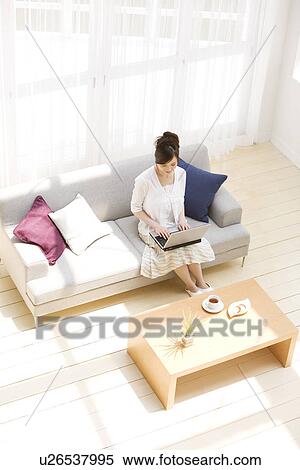 Woman using laptop on sofa in living room View Large Photo Image Stock Photography - Woman using laptop on sofa in living room. Fotosearch
