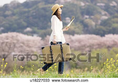 Stock Image - Woman walking with suitcase and map. Fotosearch
