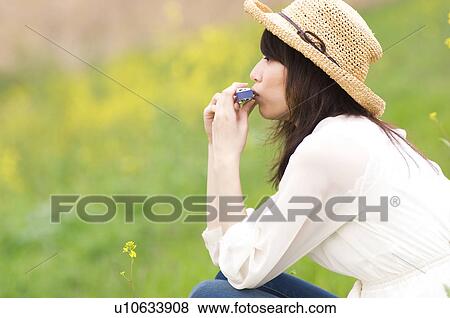 Stock Photo - Woman wearing straw hat playing harmonica in a meadow. Fotosearch