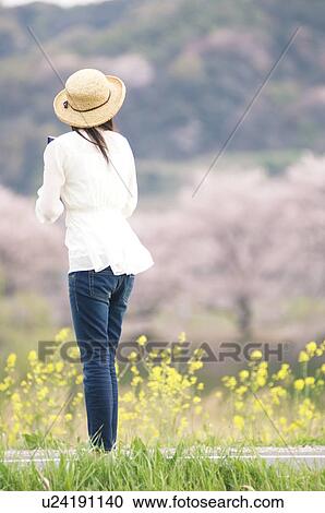 Stock Image - Woman wearing straw hat standing by roadside. Fotosearch