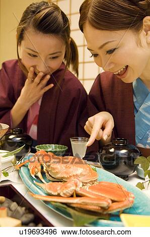 Stock Photograph - Women pointing and laughing at cooked crab on plate. Fotosearch