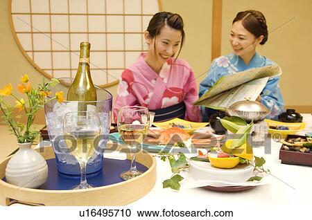 Stock Image - Women sitting at table with meal, reading map. Fotosearch