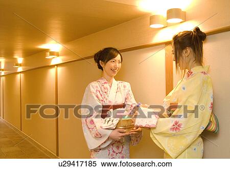 Stock Photography - Women wearing yukata standing talking in hallway of health spa. Fotosearch