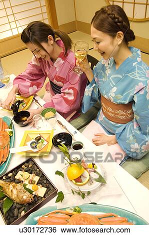 Stock Photograph - Women wearing yukatas sitting at table with seafood. Fotosearch