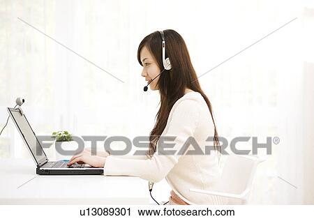 Stock Image - Young woman at computer using webcam. Fotosearch