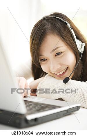 Picture - Young woman at computer with headphones. Fotosearch
