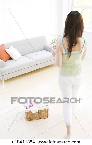 Young woman holding potted plant in living room View Large Photo Image Picture - Young woman holding potted plant in living room. Fotosearch