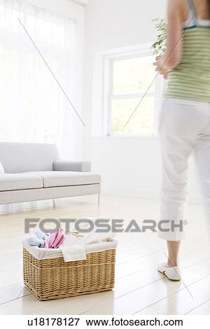 Stock Photo - Young woman holding potted plant in living room. Fotosearch