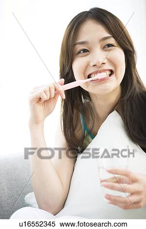 Stock Photography - Young woman sitting brushing teeth. Fotosearch