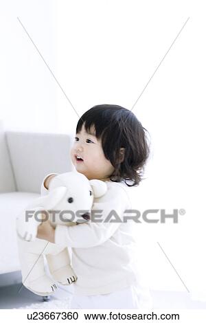 Stock Image - Baby girl carrying a teddy bear. Fotosearch