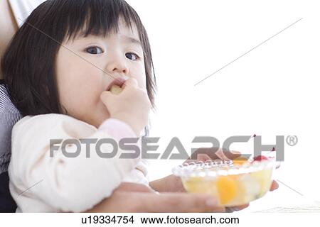 Baby girl eating fruit salad on her mother's lap View Large Photo Image Picture - Baby girl eating fruit salad on her mother's lap. Fotosearch