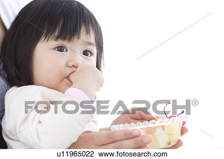 Stock Image - Baby girl eating fruit salad on her mother's lap. Fotosearch
