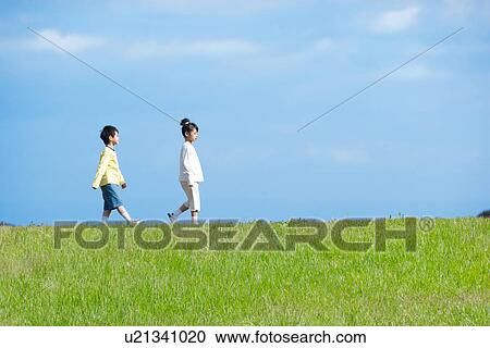 Stock Image - Brother and sister walking in the park against a blue sky. Fotosearch