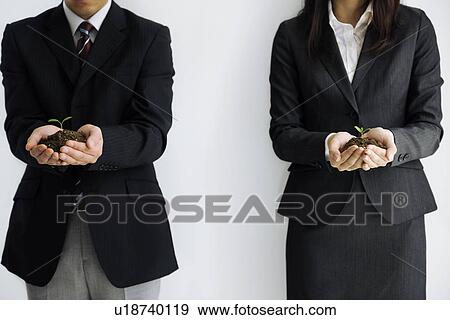Stock Photo - Businessman and businesswoman holding a seedling growing in soil. Fotosearch