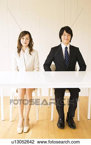 Stock Image - Businessman and businesswoman sitting at table. Fotosearch