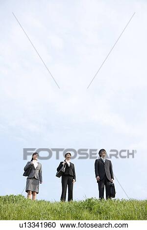 Stock Image - Businessman and businesswomen standing on grass. Fotosearch