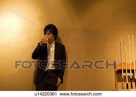 Stock Image - Businessman leaning against a wall with a drink. Fotosearch