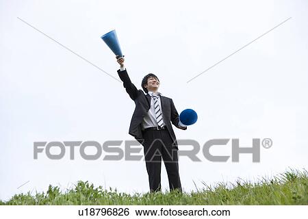 Stock Photograph - Businessman standing on grass with megaphones. Fotosearch